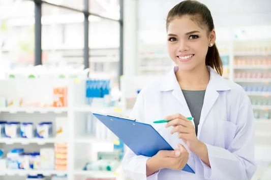 Fiatal gyógyszerész jegyzettömbbel a kezében áll a patikai polc előtt
