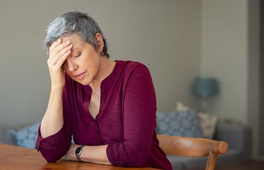 Menopausában lévő nő ül az asztalnál, kezével fejét támasztja, nem érzi jól magát
